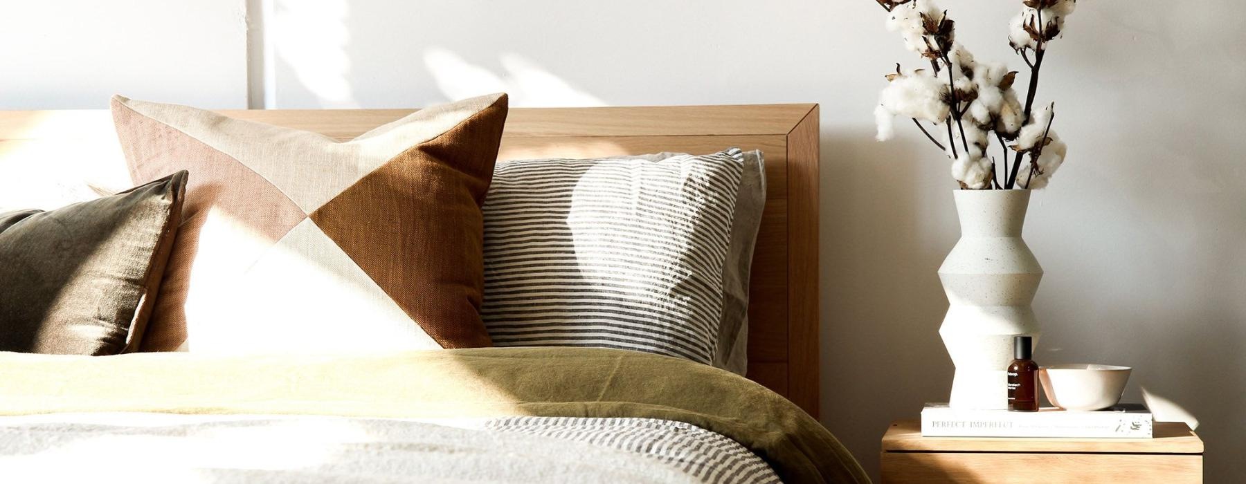 swath of sunlight shines across a well made bed and bedside table with a vase of cotton plants